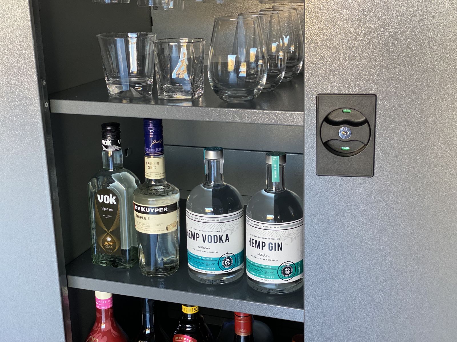 A metal cabinet with locks in a garage bar filled with top shelf spirits